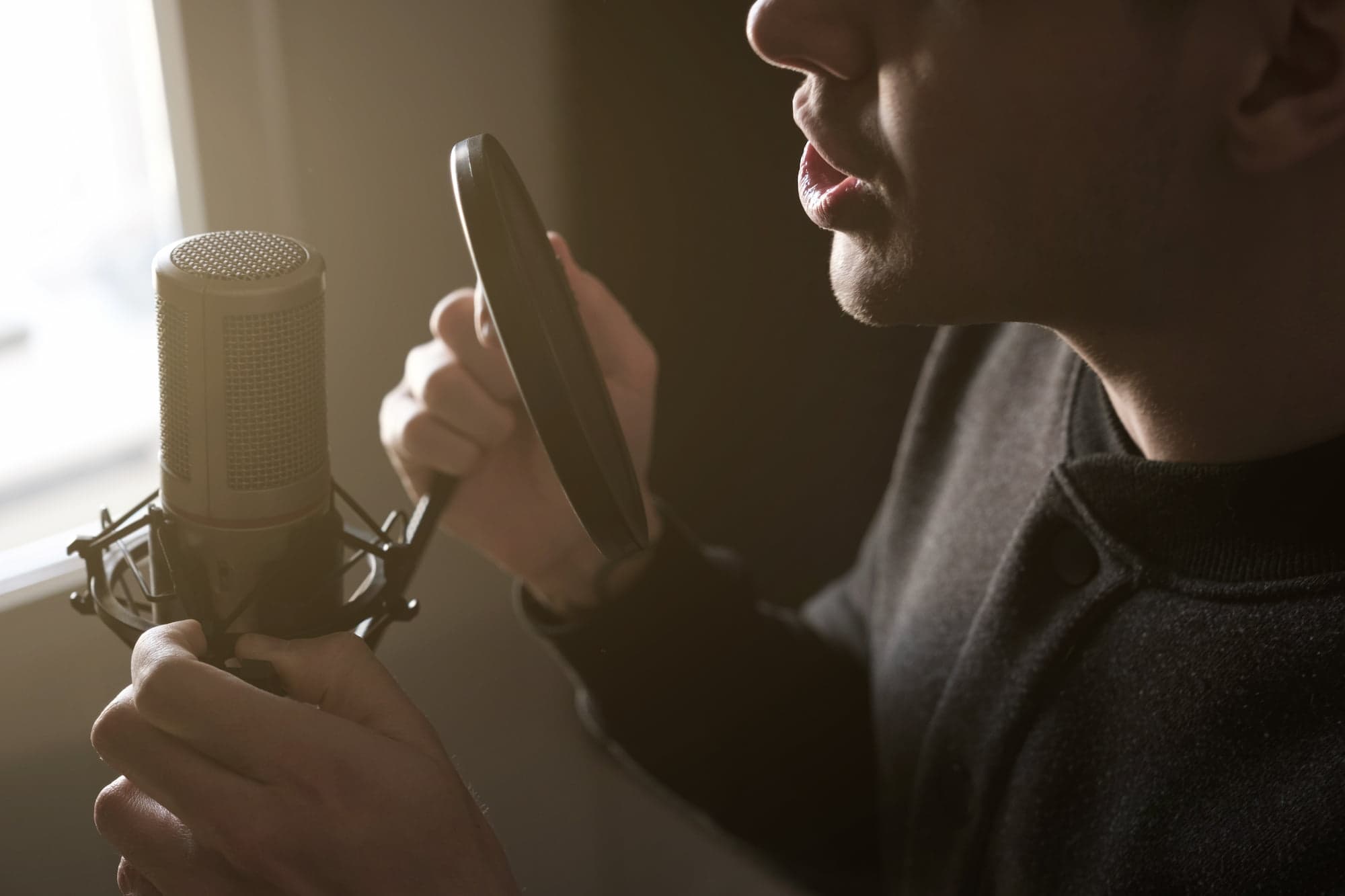 Man singing into a studio microphone with sunlight coming in through the window