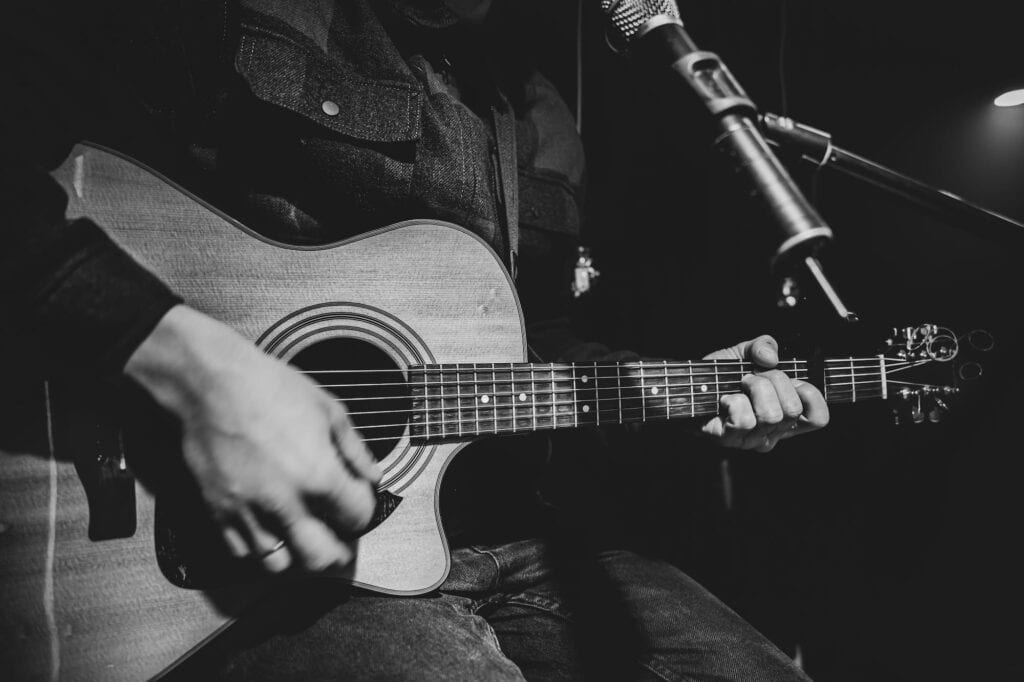 Black and white picture of a man holding a guitar and singing into a microphone at a studio