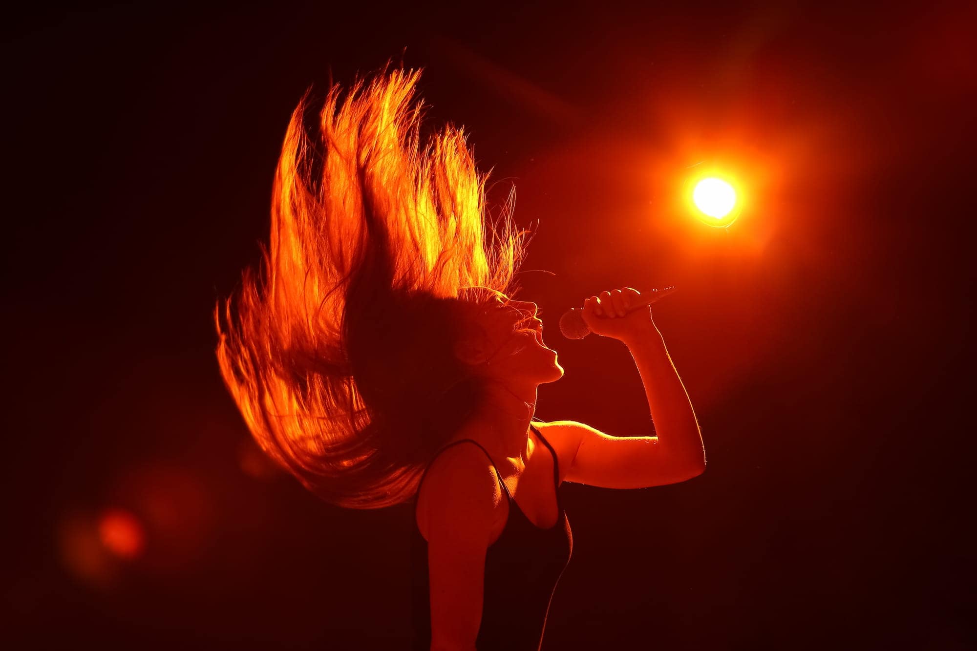 Woman flipping her hair back and singing a high night with studio lighting