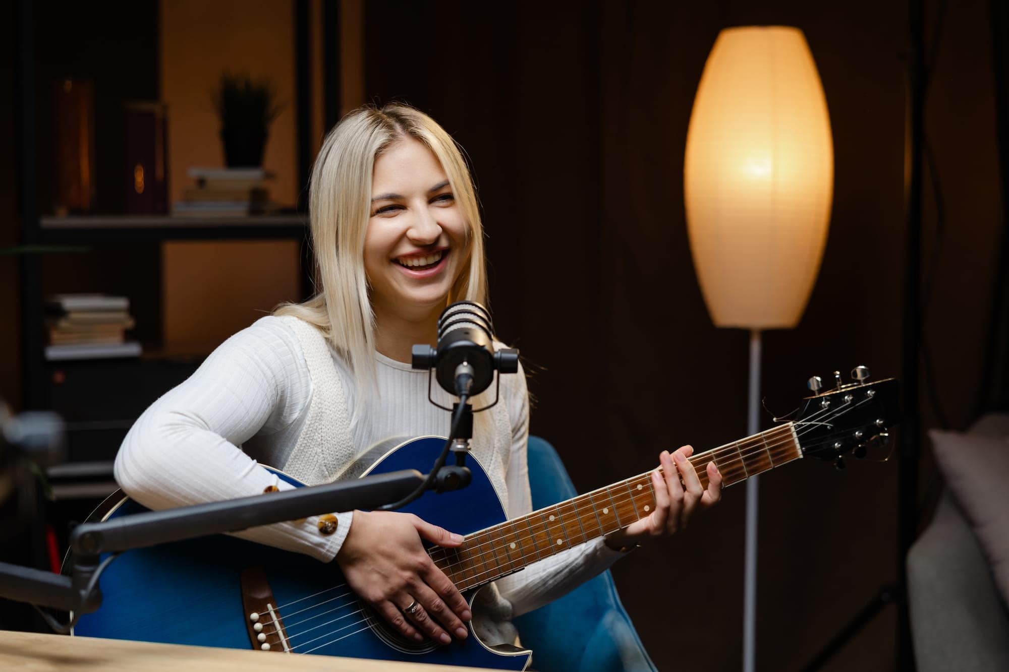 Blonde woman practicing singing and playing guitar from home